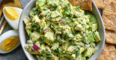 Herby avocado egg salad served in a bowl with fresh herbs and eggs.