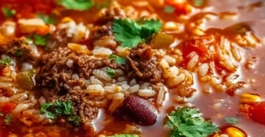 A bowl of Mexican beef and rice soup garnished with cilantro and lime